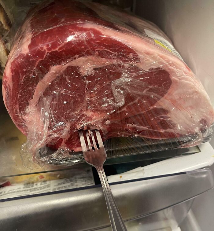 Fork stuck in raw meat wrapped in plastic, possibly leading to a Christmas accident in the kitchen.