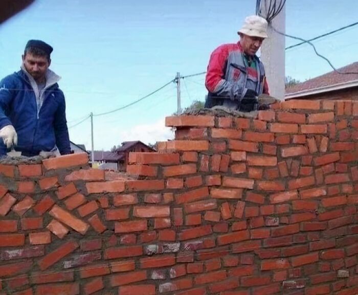 Two construction workers building a brick wall with uneven, funny cheap construction fails.