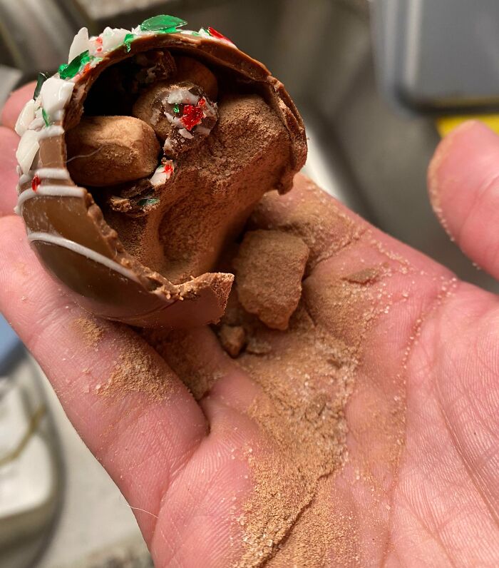 Hand holding a broken chocolate Christmas ornament, showcasing a holiday accident.