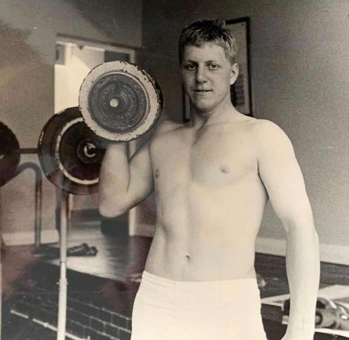 Man lifting a dumbbell in a vintage 80s gym setting, showcasing classic fitness style.