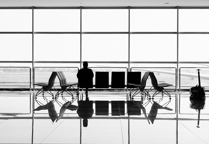 Silhouette of a person sitting in an airport with empty seats and a suitcase.