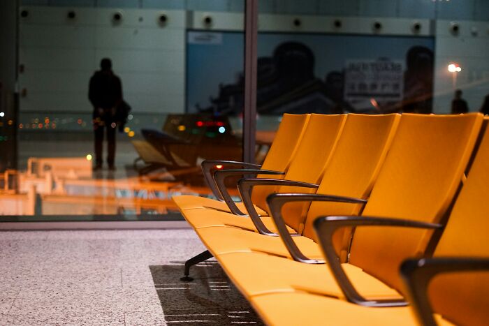 Empty airport seats with a traveler in the background.