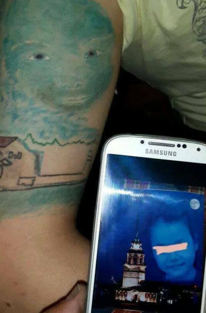 Epic tattoo fail with a blurred blue face and a building displayed on a smartphone screen below it.