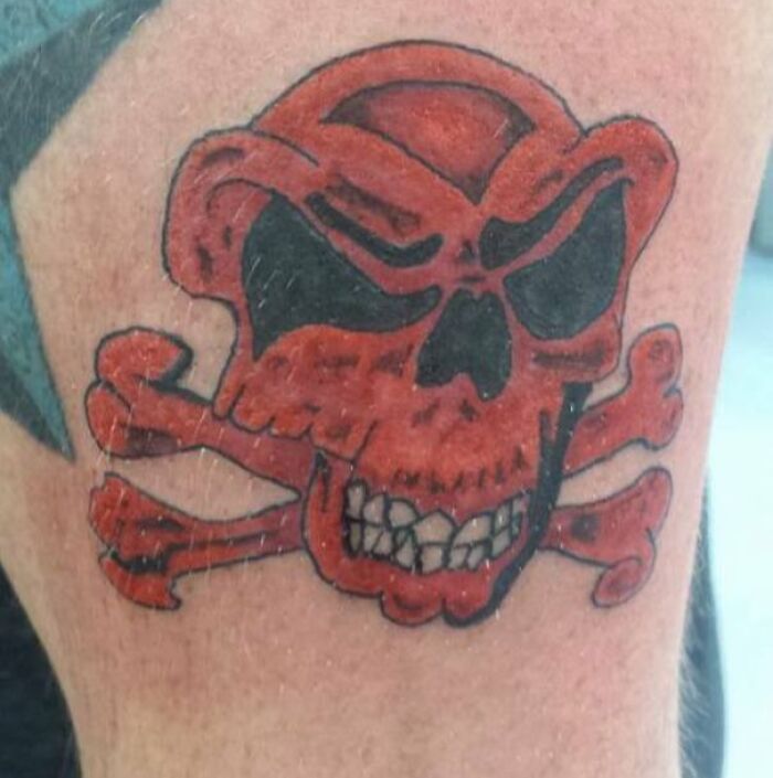 Epic tattoo fail depicting a red skull with black eyes and crossed bones on skin.