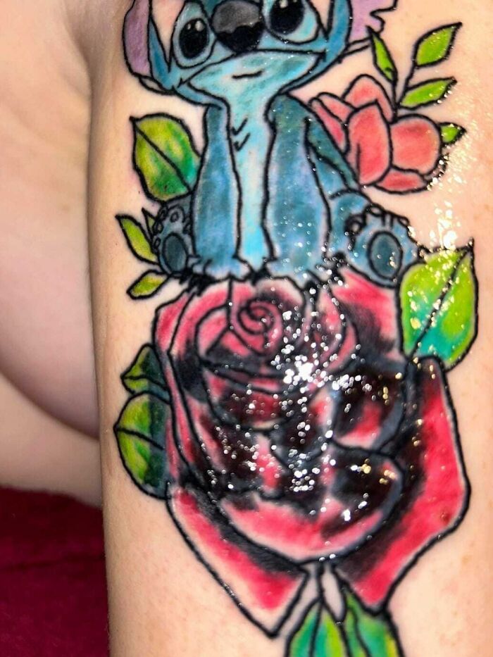 Epic tattoo fail featuring a smudged cartoon character on a colorful rose background.