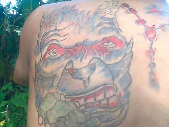 Back tattoo with a distorted face design, showcasing an epic tattoo fail, with red and blue elements.