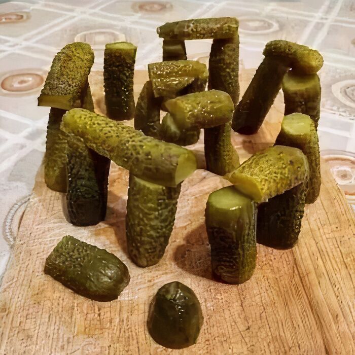 Pickles arranged like Stonehenge on a wooden board, creating a cursed image.