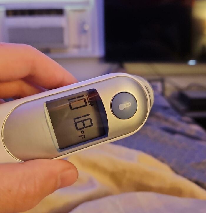 Hand holding a digital thermometer reading 101.8°F, illustrating Christmas accident or illness scenario.