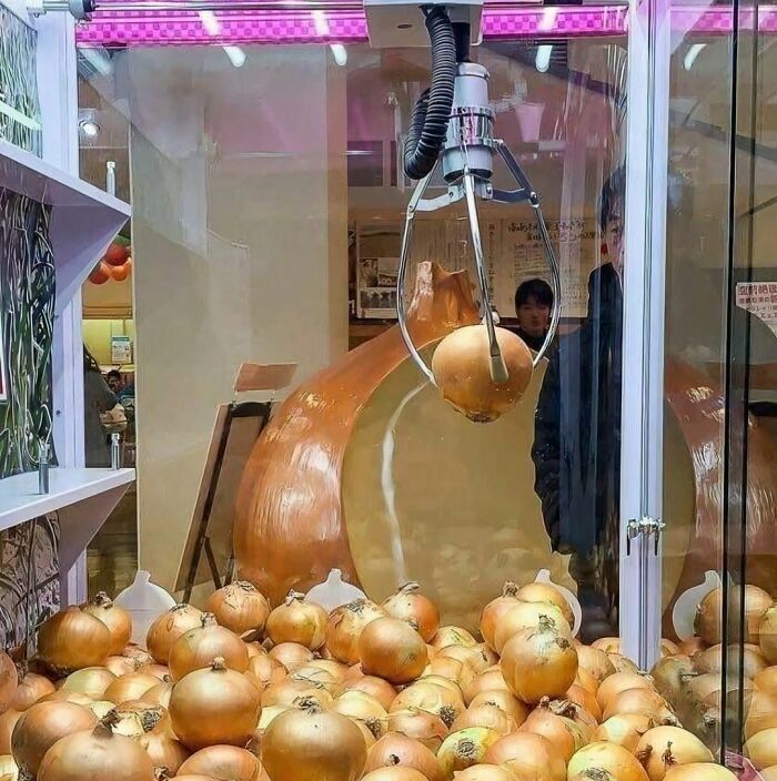 Claw machine filled with onions, capturing one, evoking imagery of cursed images.