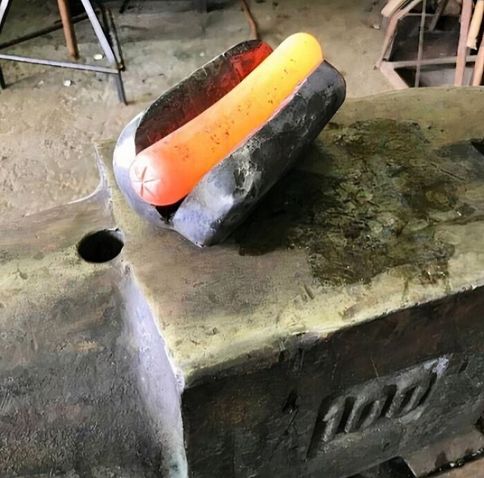 Cursed image of a glowing hot dog-shaped object resting on an anvil.