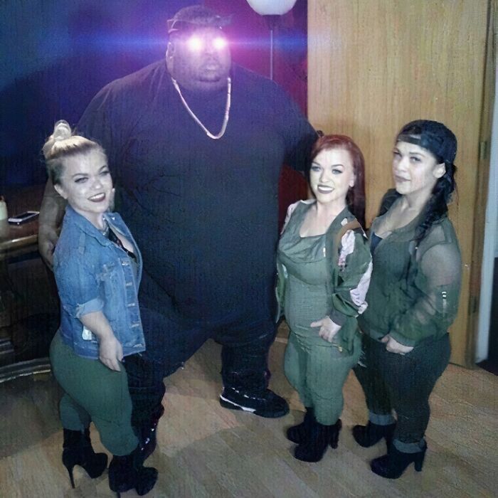 Group posing for a photo with a large man in black with glowing eyes, reflecting the IG page's style of cursed images.