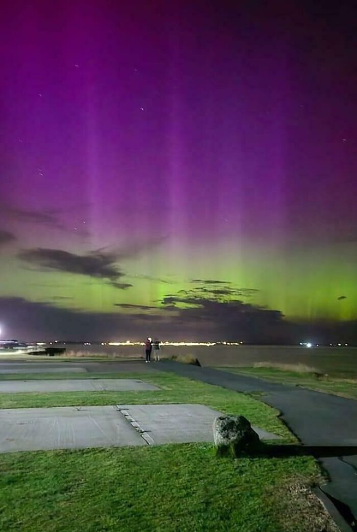 Purple and green aurora borealis illuminating the night sky over a calm landscape.