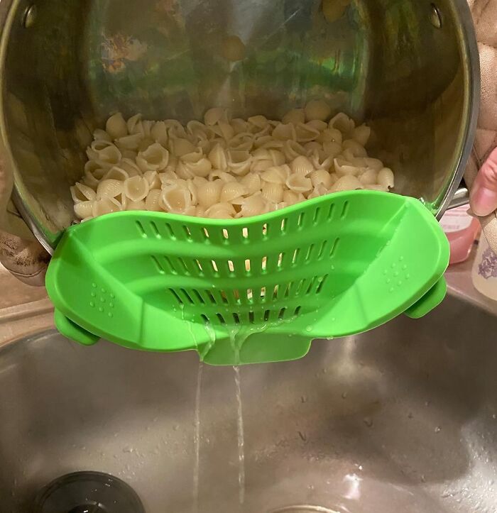 A green clip-on pot strainer being used to drain pasta shells, simplifying kitchen tasks.