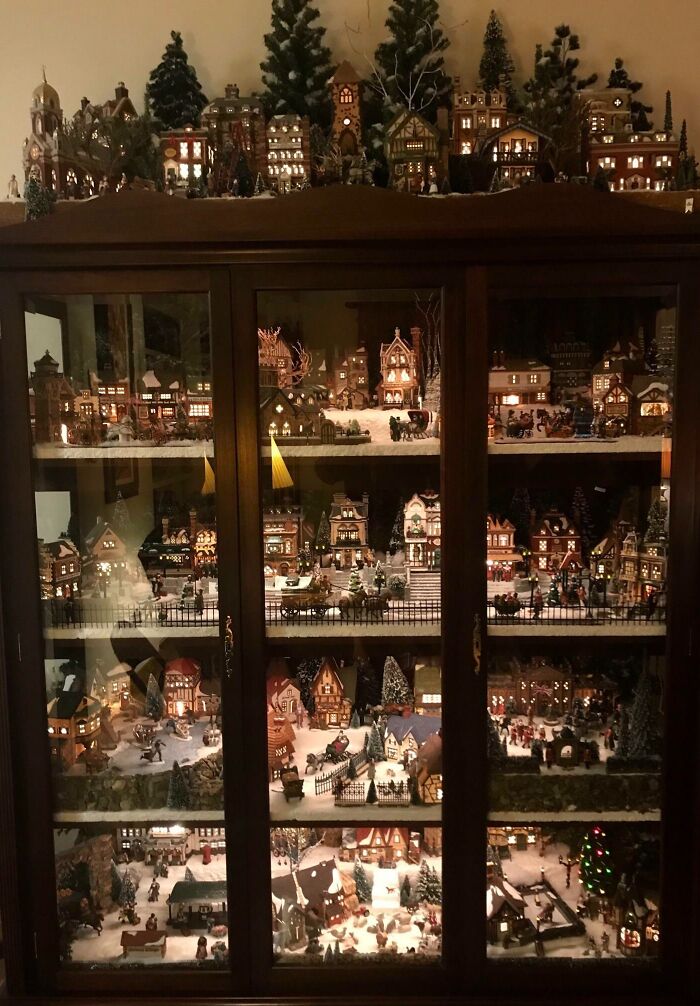 Christmas decorating ideas showcased in a cabinet with a detailed miniature village scene and glowing lights.