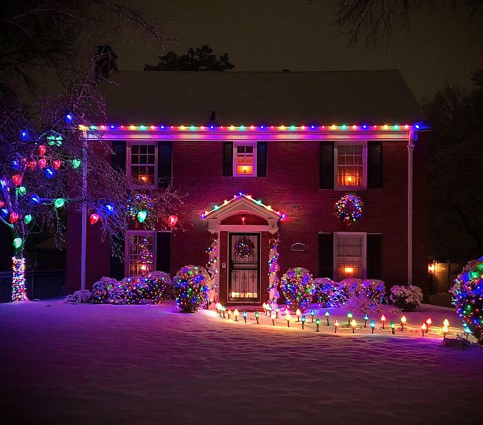 Festive house with colorful Christmas decorating ideas using lights and wreaths in a snowy setting.