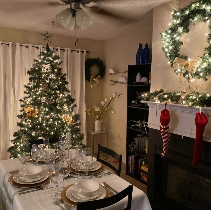 Christmas-decorating-ideas: Festive living room with lit tree, wreaths, dining table set, and stockings on a mantel.