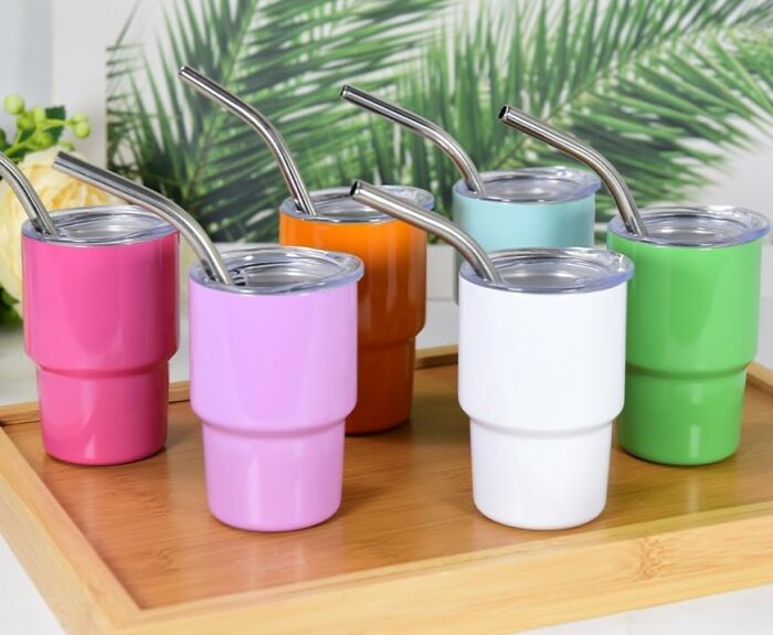 Colorful stainless steel cups with metal straws on a wooden tray, perfect for drinks.