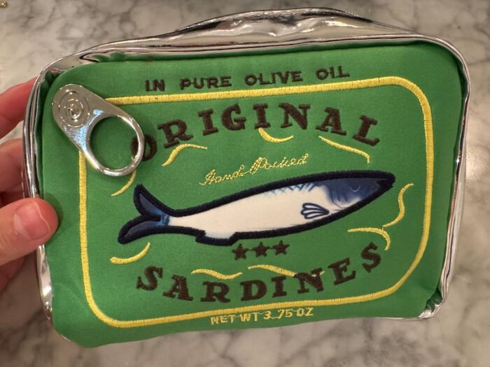 Green sardine tin purse with fish graphic and tab opener features quirky design.