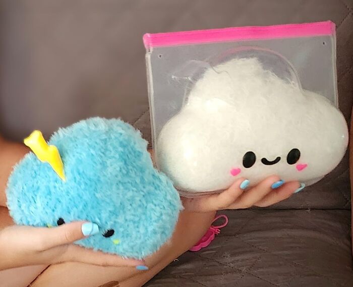 Two plush cloud toys, one blue with a yellow lightning bolt and one white with a smiling face, held in hands.