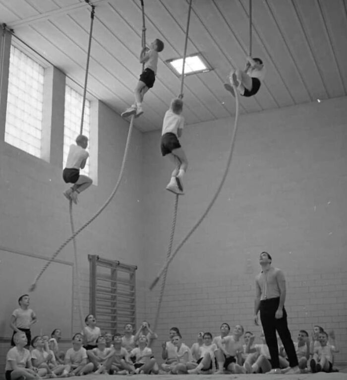 Children climbing ropes in a vintage gym class with an instructor, capturing 80s gym fitness activities.