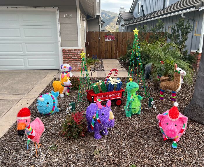 Colorful animal Christmas decorations in a yard with lighted trees and festive ornaments.