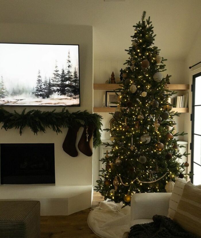 Christmas-decorating-ideas featuring a lit tree with gold ornaments beside a fireplace adorned with garland and stockings.