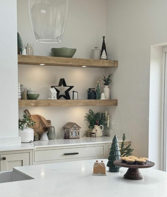 Modern kitchen with Christmas-decorating-ideas, featuring small trees, gingerbread houses, and festive ornaments on shelves.