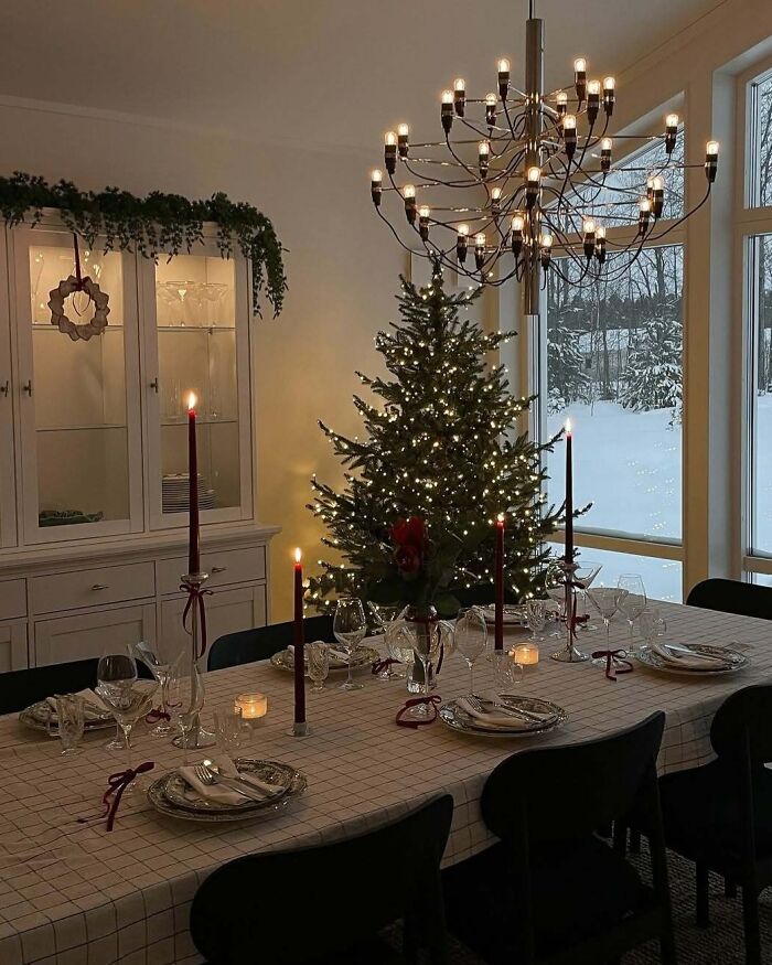 Christmas-decorating-ideas with a beautifully set dining table, festive tree, and elegant chandelier lighting.