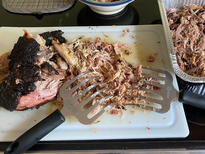 Meat shredding tool on a cutting board with pulled pork, showcasing clever inventions for easier kitchen tasks.