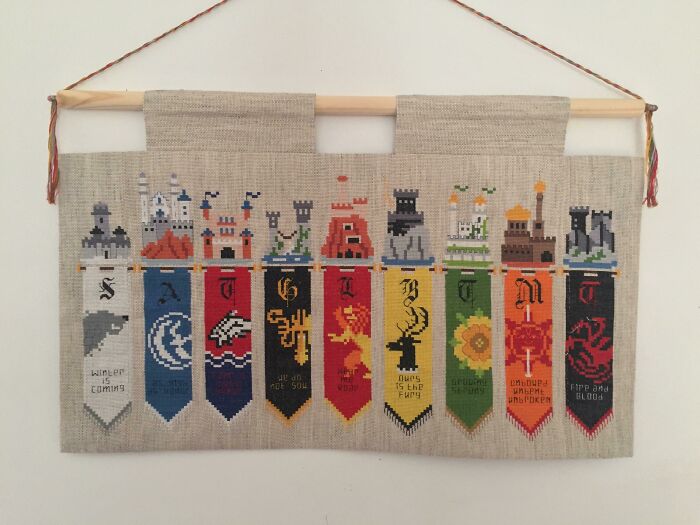 Colorful cross-stitched Game of Thrones banners hanging on a wall, showcasing various house sigils and mottos.