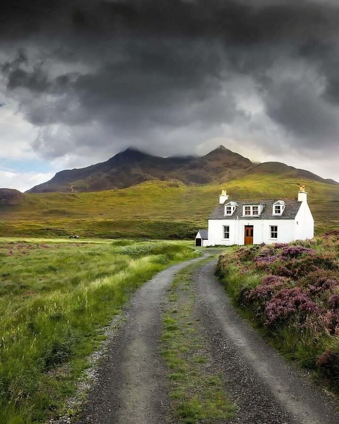 A charming Scottish cottage with a winding path and dramatic hills in the background.