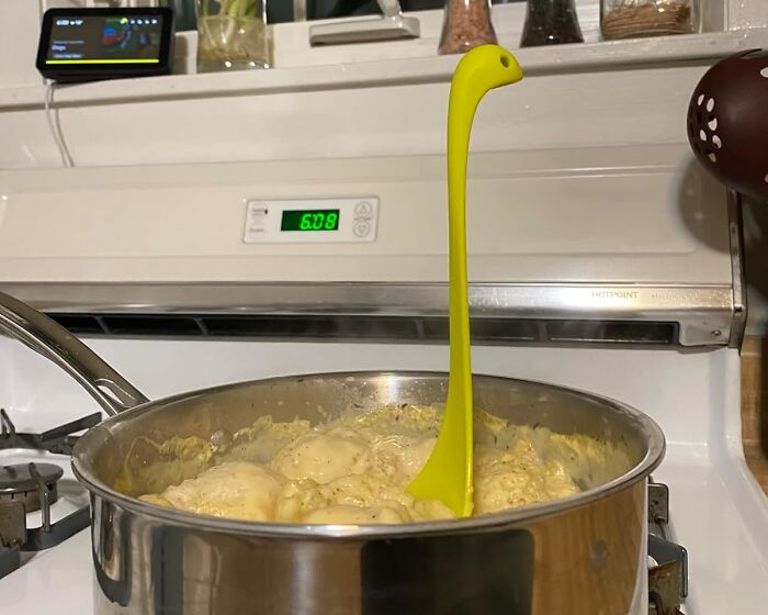 A quirky dinosaur-shaped ladle in a pot on the stove, showcasing a kitchen item some will love or hate.