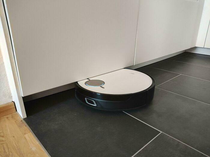 A robot vacuum fitting perfectly under a cabinet on a tiled floor.