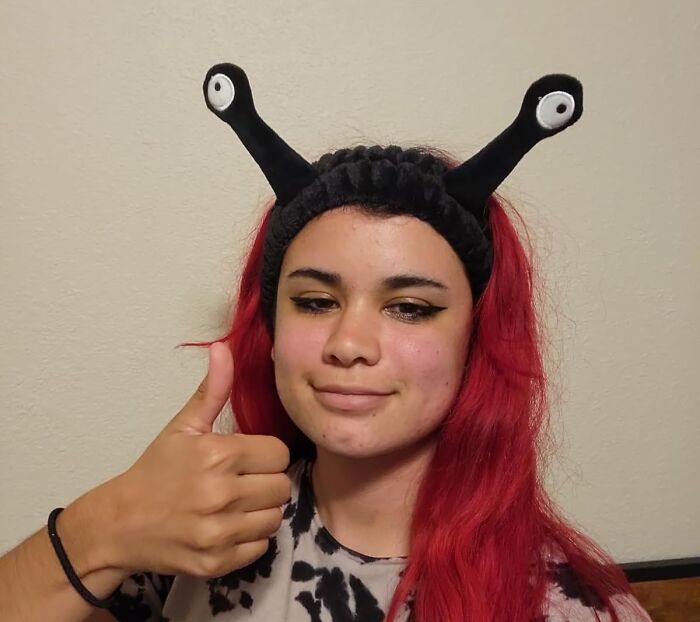 Person with red hair wearing funny antenna headband, giving a thumbs up.