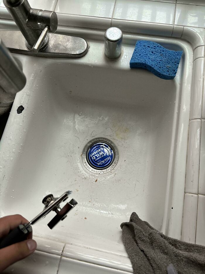 A perfectly fitting can lid snugly placed in the kitchen sink drain, next to a blue sponge and faucet.