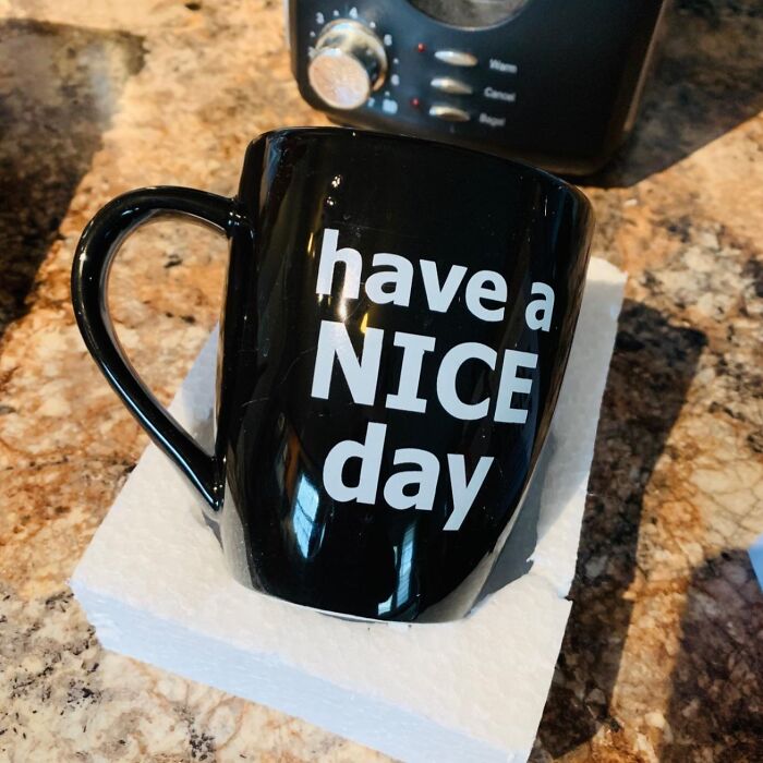 Black mug with "have a NICE day" text, ideal for White Elephant Gifts, on a kitchen counter.