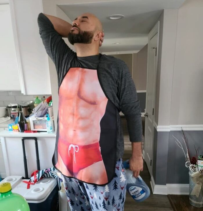 Man wearing a novelty apron depicting a muscular torso, suitable as a humorous white elephant gift.