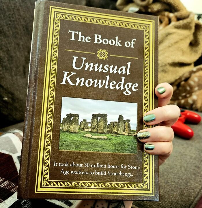 Person holding "The Book of Unusual Knowledge," a fun choice for white elephant gifts.