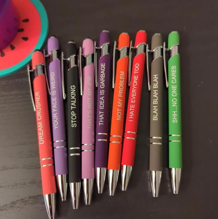 White Elephant Gifts: colorful pens with humorous phrases in a playful arrangement on a dark table.