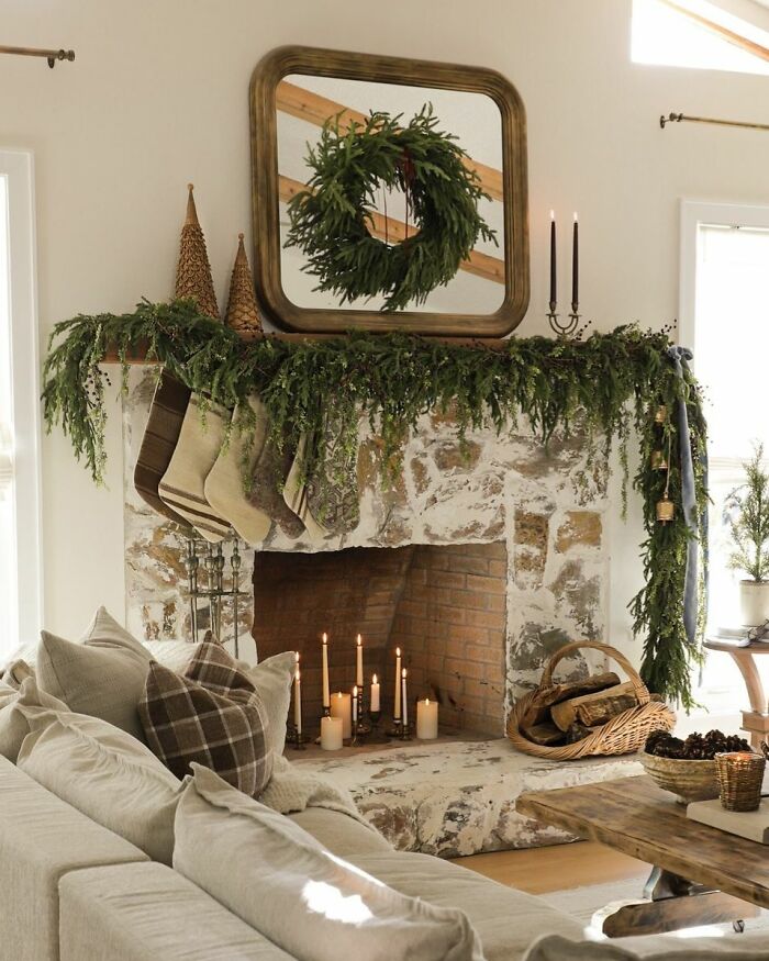 Christmas-decorating-ideas with a wreath above a rustic mantel adorned with garlands, stockings, and lit candles.