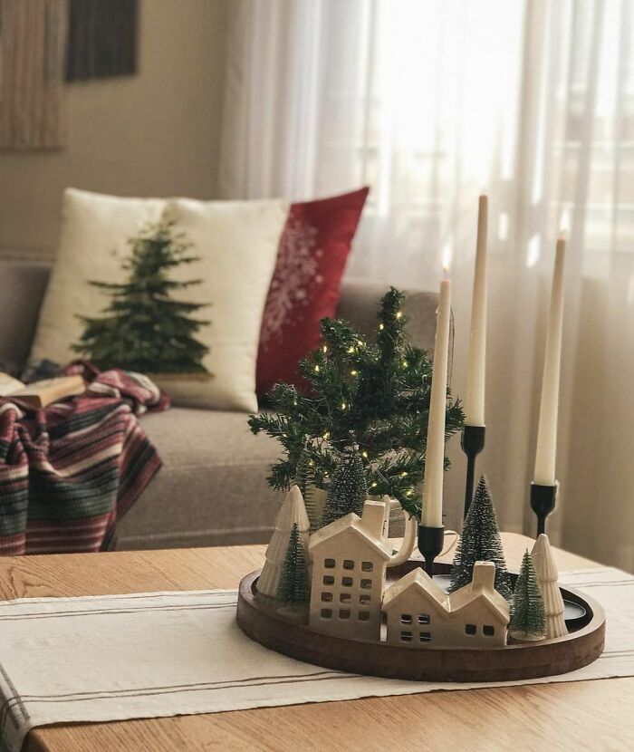 Christmas-decorating-ideas with miniature houses, trees, and candles on a wooden table centerpiece in a cozy living room.