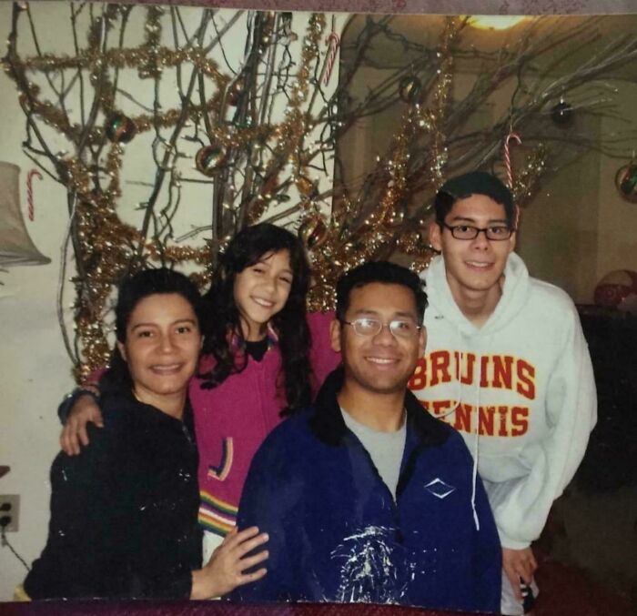 Smiling family posing in front of a Christmas tree with homemade decorations, capturing a wholesome Christmas moment.