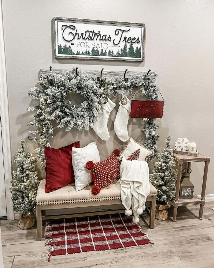 Christmas-decorating-ideas with frosted wreath, stockings, red and white pillows on a bench, and a "Christmas Trees For Sale" sign.