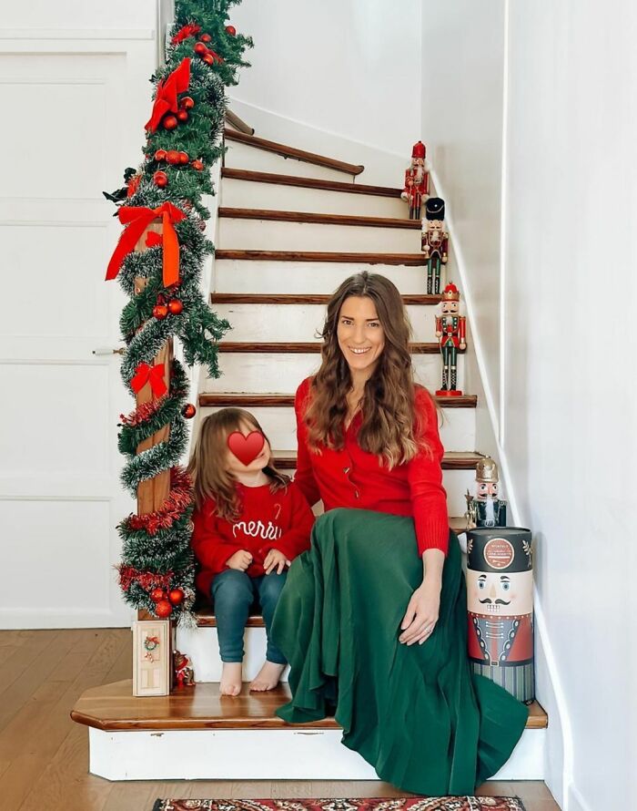 A woman and child in festive clothes on stairs decorated with Christmas garland and nutcrackers; Christmas decorating ideas.