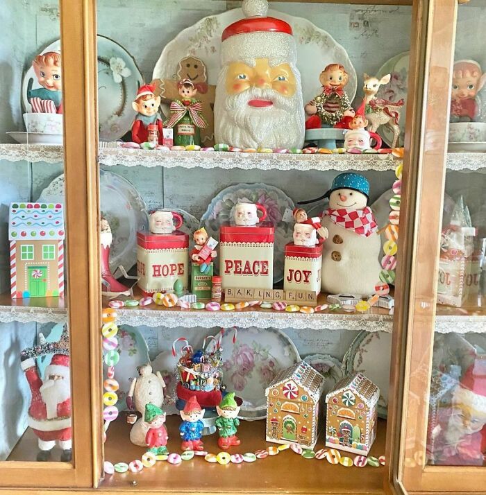 Festive Christmas-decorating-ideas with vintage figures, Santa, snowman, joy canisters, and gingerbread houses in a cabinet.