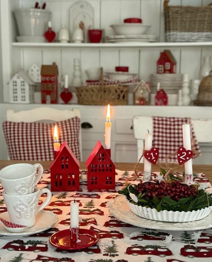 Christmas decorating ideas with red candles, festive houses, and greenery on a dining table.