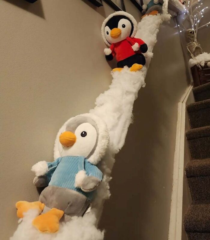 Stuffed penguins in winter clothes sliding down a snowy stair banister, showcasing Christmas decorating ideas.