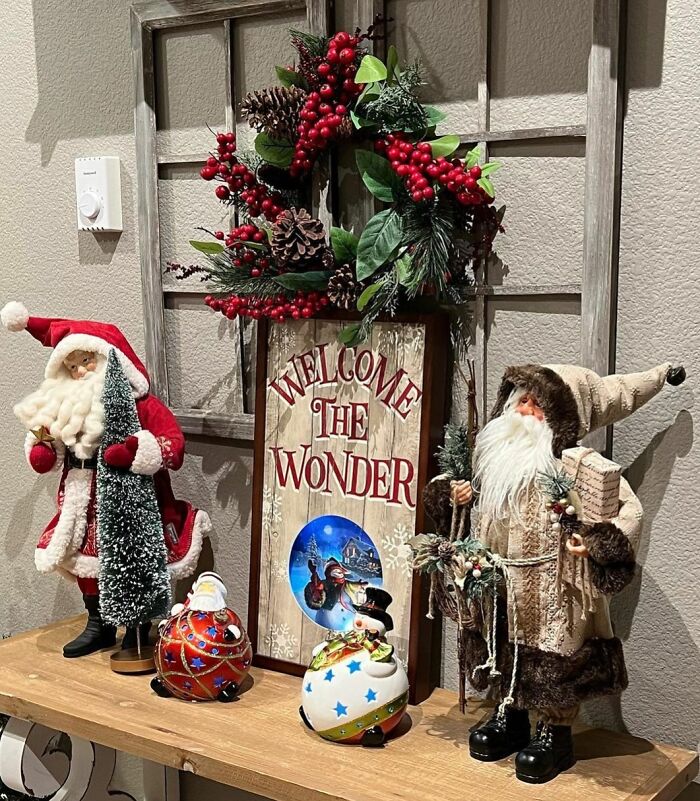 Festive Christmas decorating ideas with Santa figurines, a wreath, and a "Welcome the Wonder" sign on a wooden shelf.