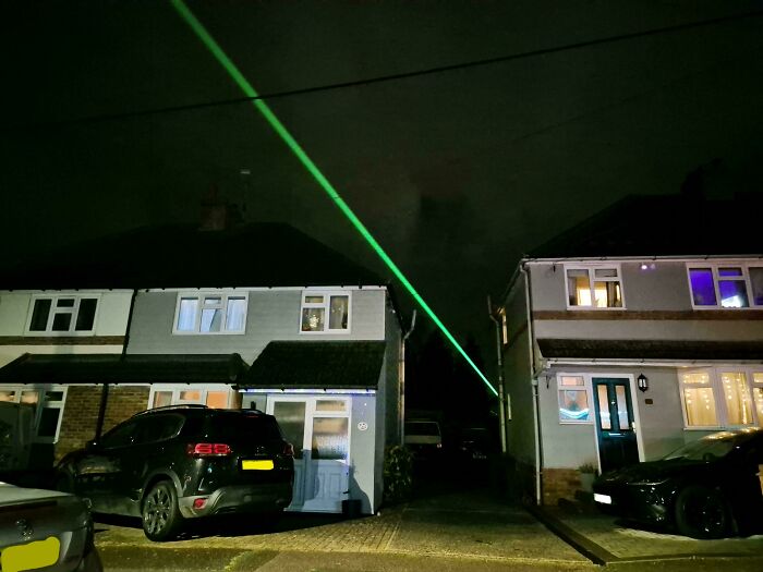 Nighttime street scene with green laser beam in the sky, creating a real-life look that resembles videogame graphics.