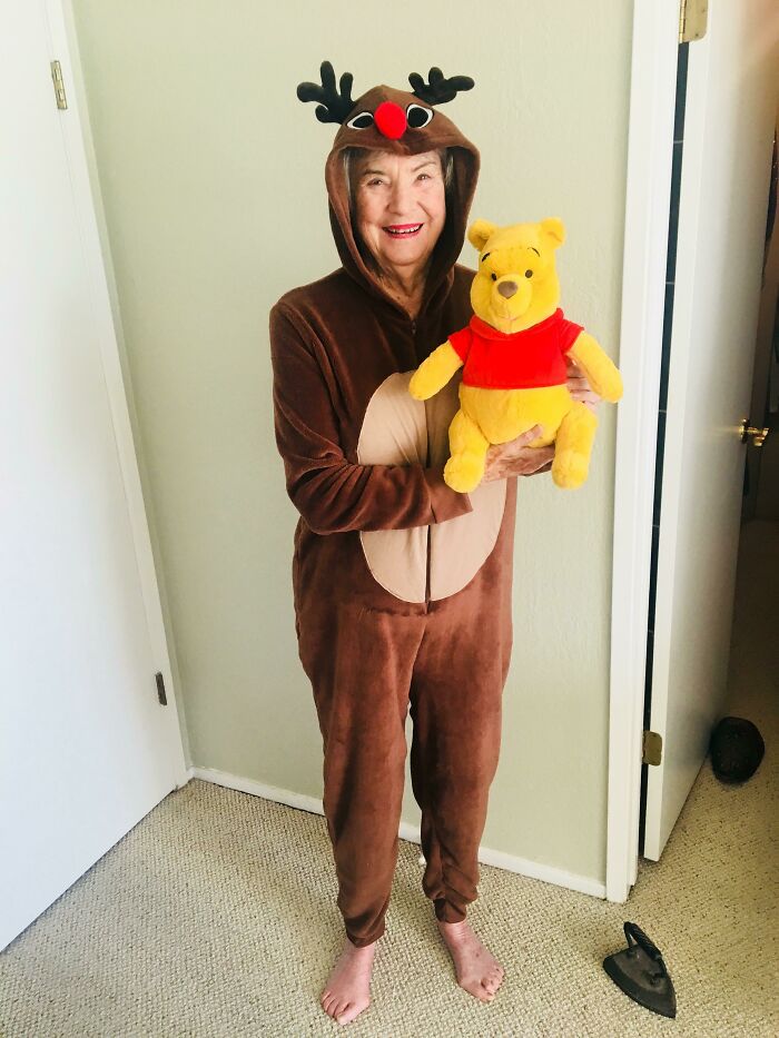 A woman in a reindeer costume smiling and holding a Winnie the Pooh plush, highlighting a wholesome Christmas moment.